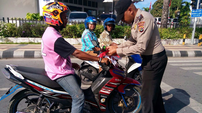 salah satu anggota polisi bagiakan bendera kepada pengendara motor di Biak